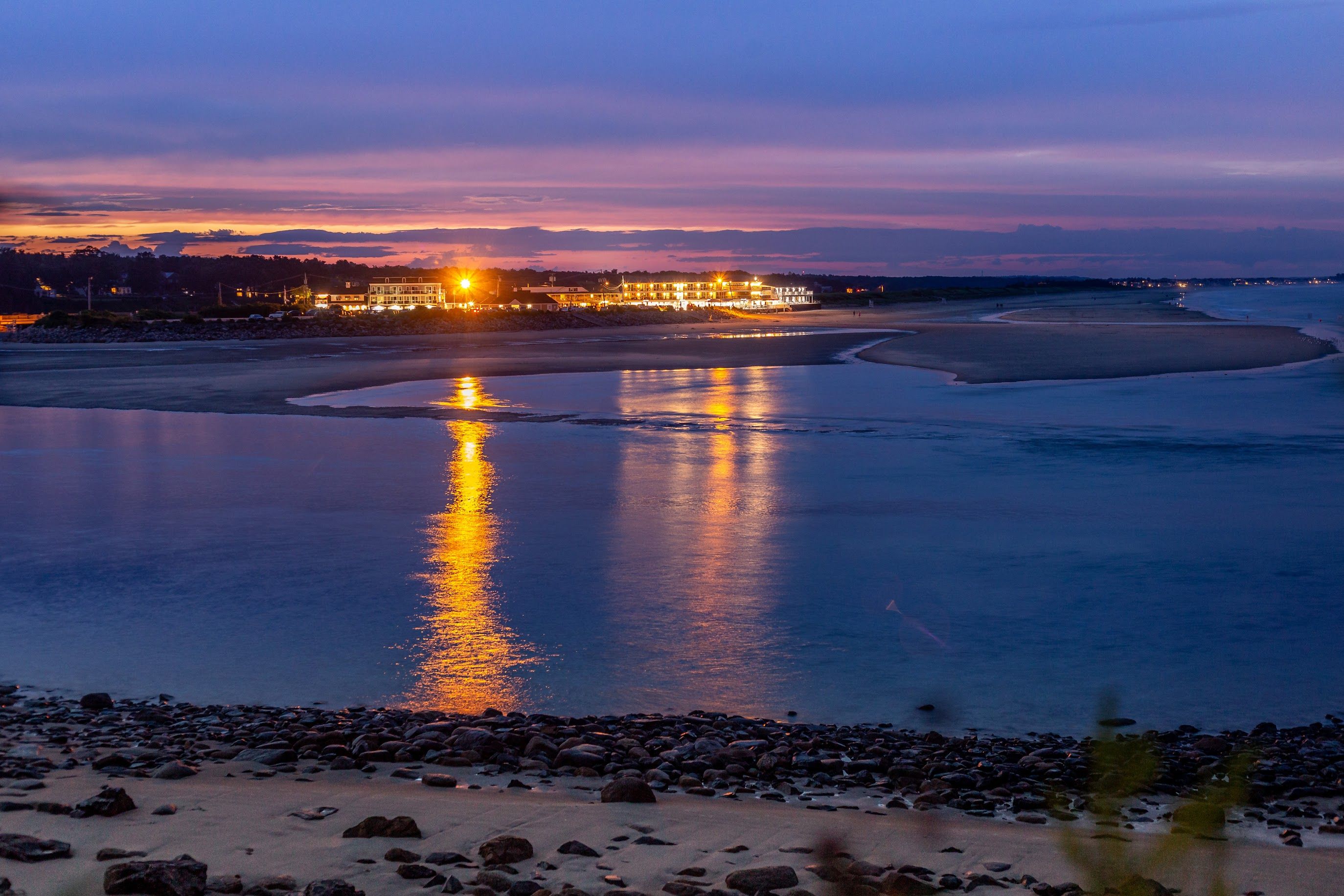 A serene coastal town at sunset, with calm waters reflecting the sky's vibrant colors.